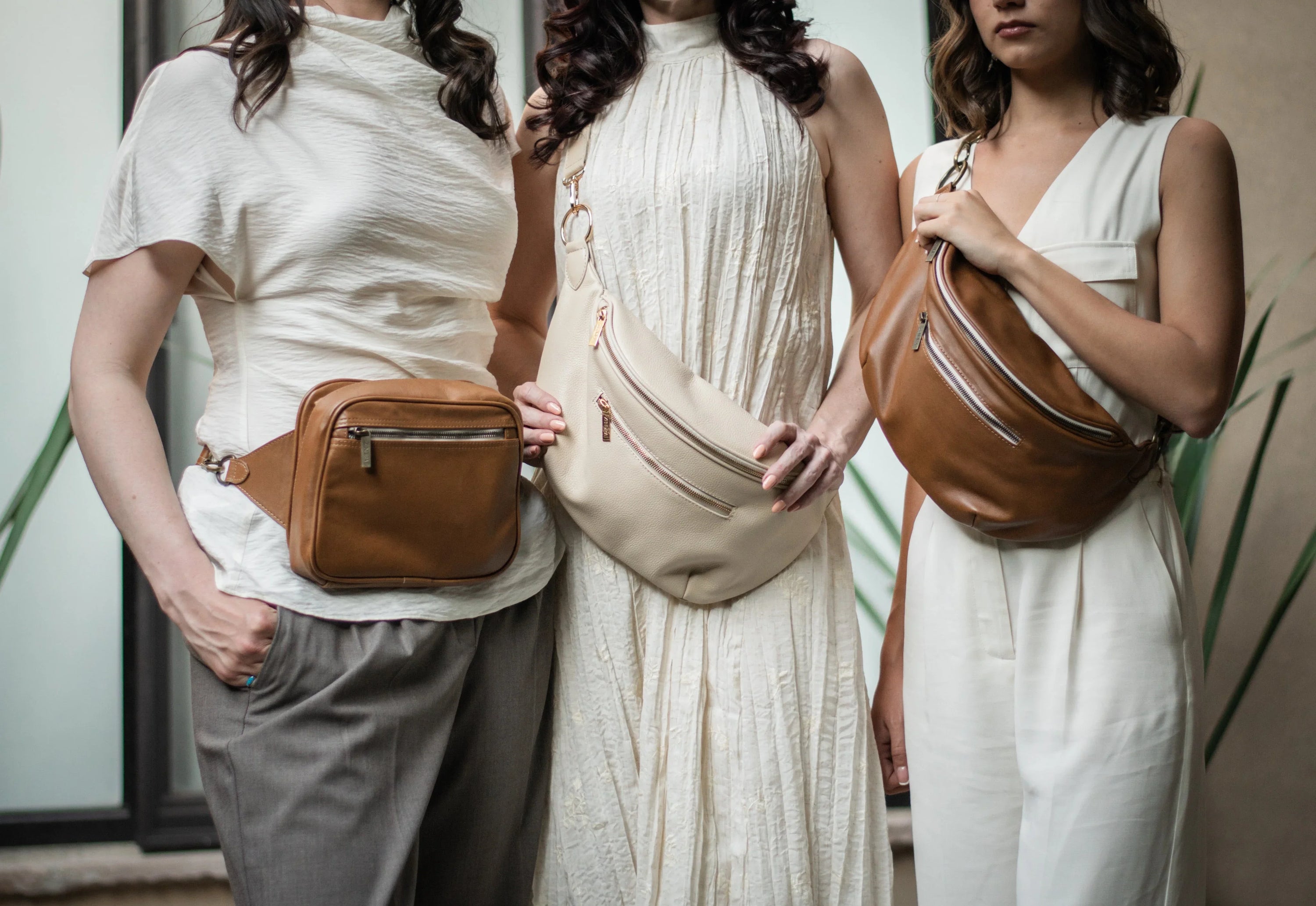 Three women modeling Zendira crossbody concealed carry bags in camel and cream tones, showcasing different sizes and carry styles in a modern, minimalist setting.