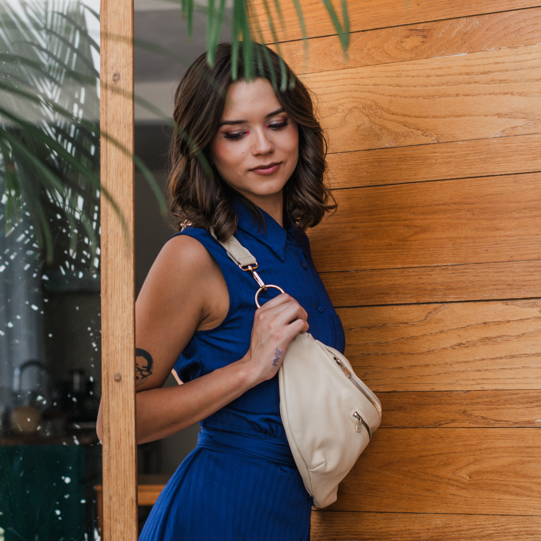 Woman in a blue dress holding a pearl Zendira Saturday concealed carry handbag against a wooden wall.
