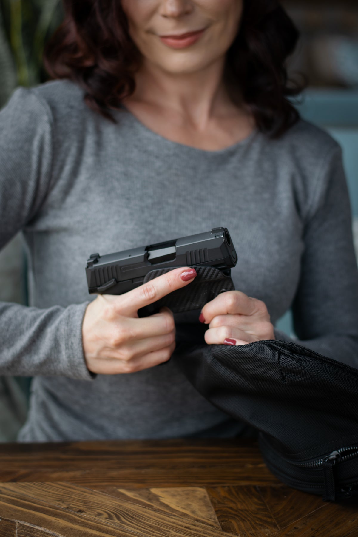 Woman holding a firearm and attaching a kydex trigger guard from inside her Zendira concealed carry bag.